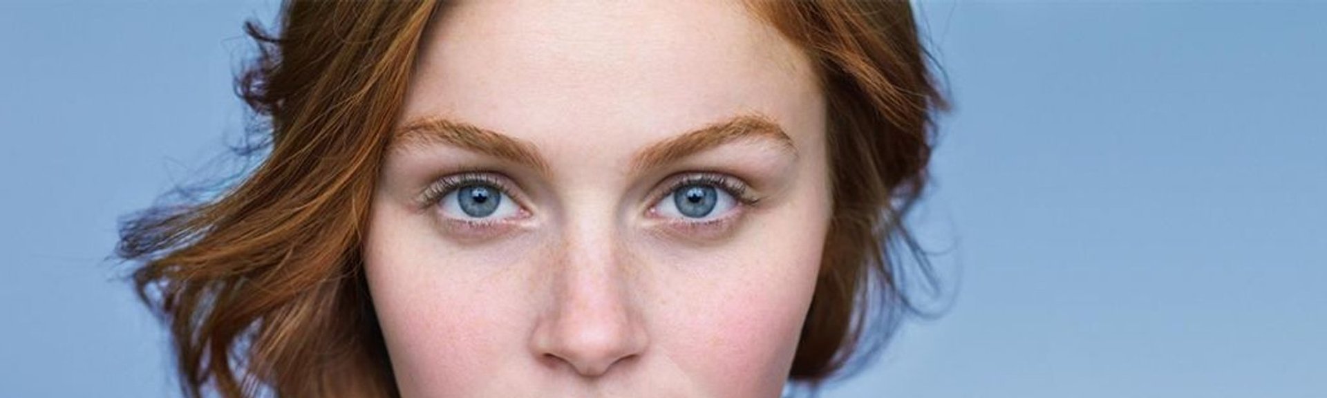 En rødhåret kvinde med blå øjne og synlig rødme på kinderne, typisk for hud med tendens til rosacea
